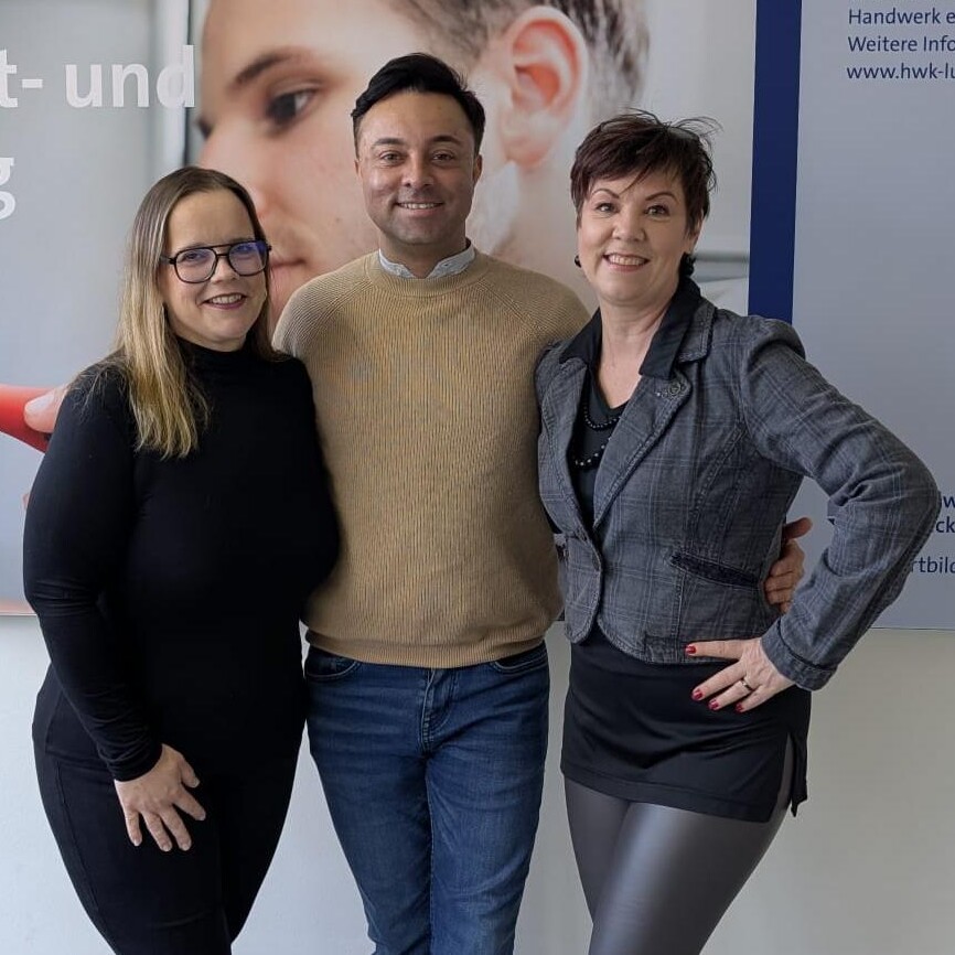 KI generiert: Eine Gruppe von drei Personen posiert lächelnd vor einem Hintergrund, der teilweise beschriftet ist.