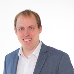 KI generiert: Das Bild zeigt einen lächelnden Mann in einem blauen Anzug vor einem hellen Hintergrund.