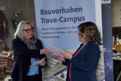 KI generiert: Zwei Personen stehen vor einem Poster, das ein Bauvorhaben für ein neues Bildungszentrum, den Trave-Campus, ankündigt.