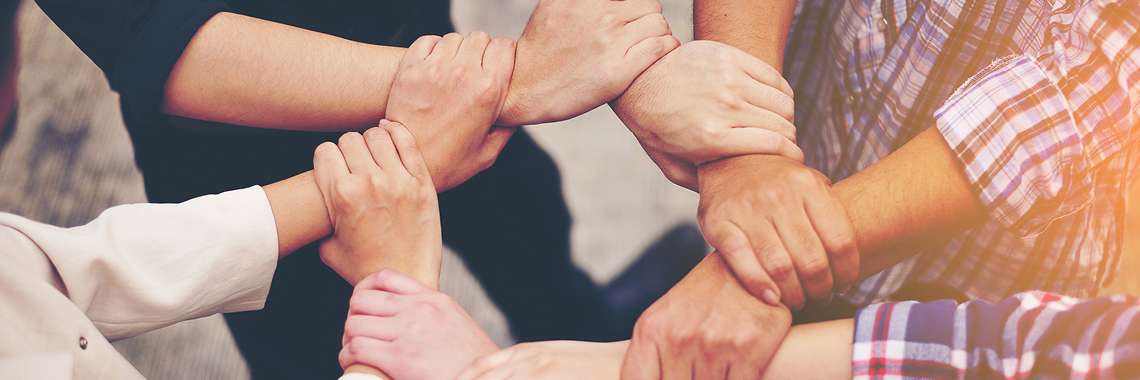Vier Personen greifen aneinander und halten deren Handgelenke fest und bilden einen Kreis