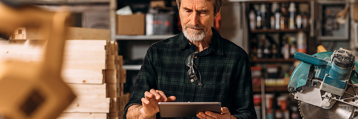 Älterer Herr in einer Werkstatt arbeitet an einem Tablet