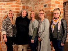 KI generiert: Eine Gruppe von fünf Frauen steht lächelnd vor einer Backsteinwand.