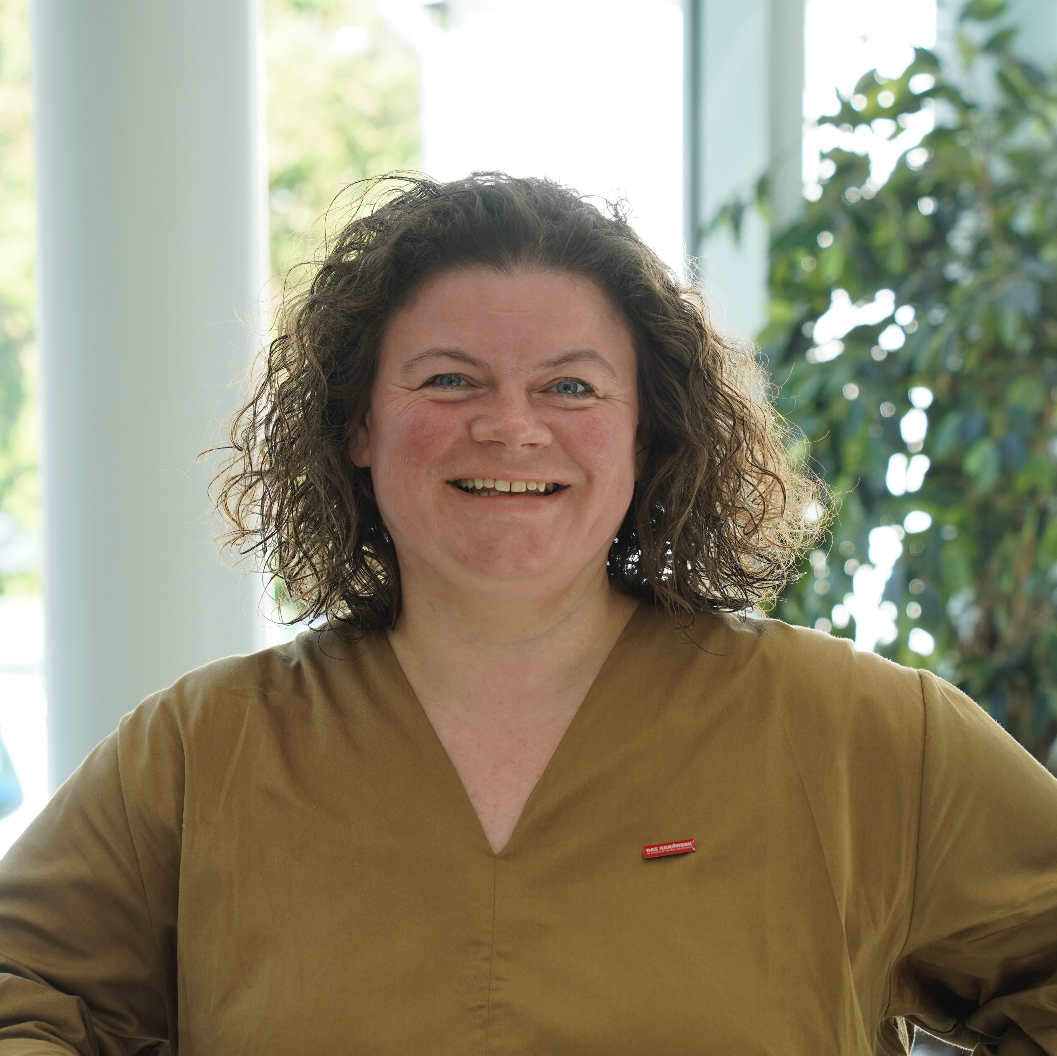 KI generiert: Das Bild zeigt eine lächelnde Frau vor einer natürlich beleuchteten Hintergrundkulisse.